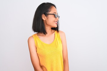 Young beautiful chinese woman wearing thug life sunglasses over isolated white background looking away to side with smile on face, natural expression. Laughing confident.