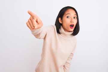 Young chinese woman wearing turtleneck sweater standing over isolated white background Pointing with finger surprised ahead, open mouth amazed expression, something on the front