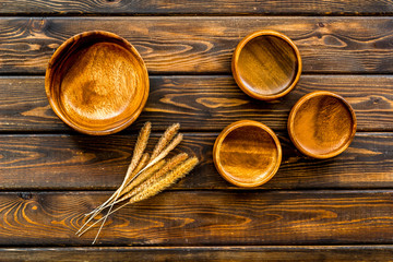 Fototapeta na wymiar Wooden bowls and ears of wheat on dark wooden background top view