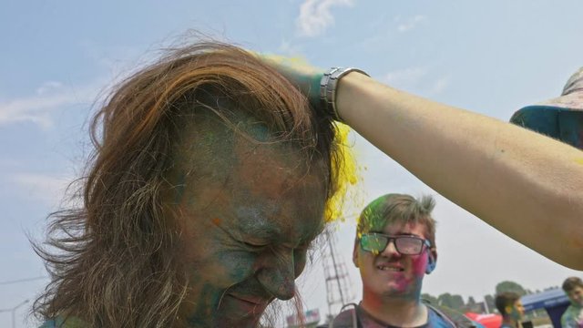 Young happy man with unfastened long hair in colourful powder is take shooting video selfie on holi festival in daytime in summer. Happy young people dancing, celebrating during Holi Festival Colors.