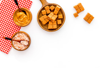 Cook salted caramel. Scoop with sweet cubes, melted caramel and salt on white background top view copy space