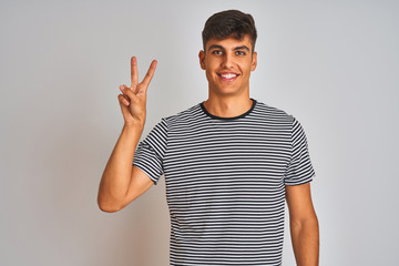 Young indian man wearing navy striped t-shirt standing over isolated white background showing and pointing up with fingers number two while smiling confident and happy.