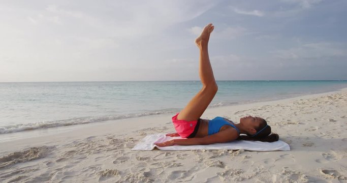 Fitness woman training working out on beach outdoors doing Lying Leg Raise With a Hip Thrust. Girl on beach training obliques stomach muscles core body training. Fit girl exercising doing abs exercise