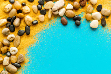 Resort or vacation concept. Sea stones and sand on blue background top-down frame copy space