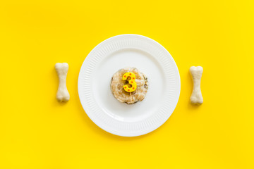 Birthday party for puppy concept. Dog feed, candle in shape of number three, bones on yellow background top-down