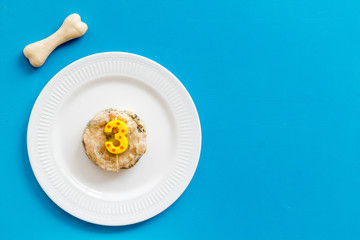 Birthday treat for puppy concept. Dog feed, candle in shape of number three, bones on blue background top-down copy space
