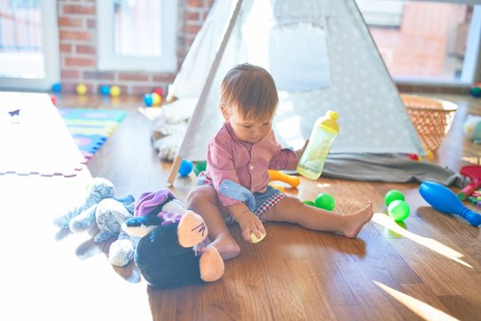 Adorable toddler holding feeding bottle around lots of toys at kindergarten