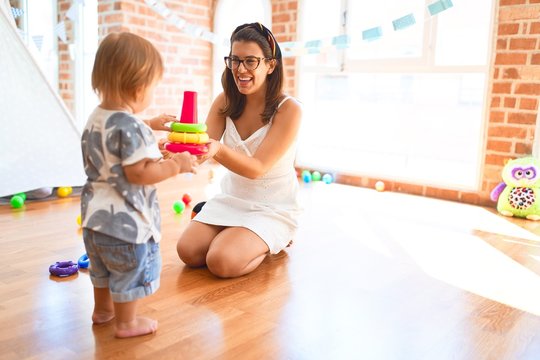 Beautiful teacher and toddler building pyramid using hoops around lots of toys at kindergarten