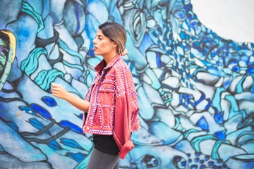 Fototapeta premium Young beautiful girl wearing red jacket standing backwards over colorful wall at the town street