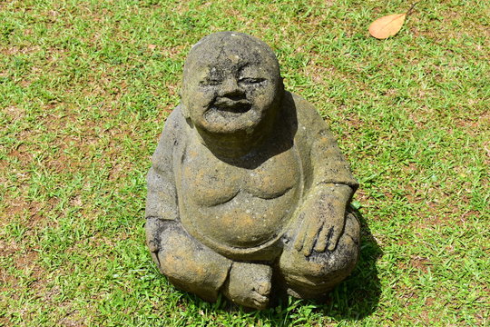 Beautiful picture of laughing Buddha statue sitting on the grass, garden decoration with an asian touch.