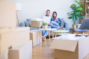 Young beautiful couple sitting on the sofa at new home around cardboard boxes
