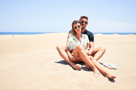Young beautiful couple smiling happy and confident. Sitting with smile on face hugging at the beach