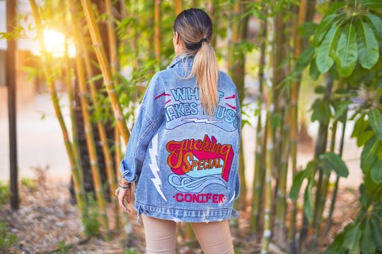 Young beautiful woman wearing denim jacket standing backwards at the town park