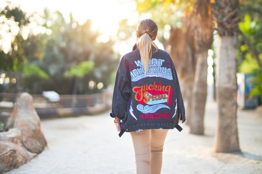 Young beautiful woman wearing denim jacket standing backwards at the town park