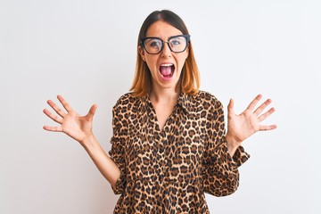 Beautiful redhead woman wearing glasses and elegant animal print shirt over isolated background celebrating crazy and amazed for success with arms raised and open eyes screaming excited.