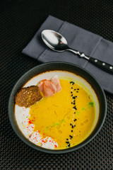 A black plate of orange pumpkin soup, spoon on the napkin