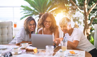 Meeting of middle age women having lunch and drinking coffee. Mature friends smiling happy using laptop at home on a sunny day
