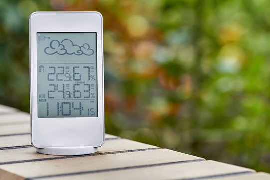 Best personal weather station device with weather conditions inside and outside on foliage background. Home digital weather forecast concept with temperature and humidity.