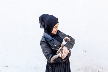 Beautiful middle-eastern Muslim woman plays with her exotic domestic Siamese cat outdoors. Pet-loving concept