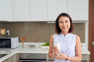 Beautiful young Asian woman drinking milk in the kitchen at home.