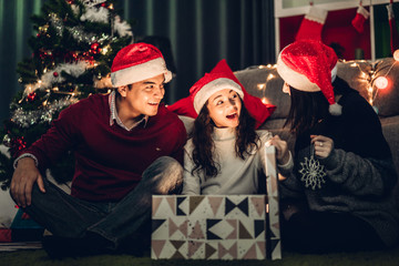 Portrait of happy family father and mother with daughter in santa hats having fun opening magic...