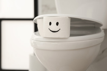 Roll of paper with funny face on toilet bowl in bathroom