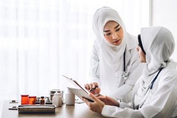 Two muslim asian female doctor working with clipboard and tablet computer on desk in hospital.healthcare and medicine