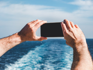 Fashionable man holding a mobile phone on the empty deck of a cruise liner against the backdrop of...