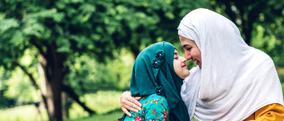 Portrait of happy lovely family arabic muslim mother and little muslim girls child with hijab dress smiling and having fun hugging and kissing together in summer park