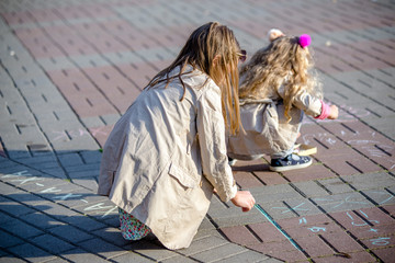 Two girls draw with chalk on the asphalt