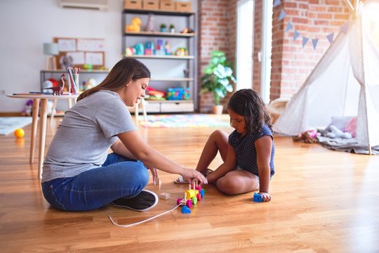 Beautiful teacher and toddler girl playing with train at kindergarten