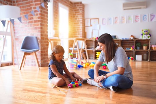 Beautiful teacher and toddler girl playing with train at kindergarten