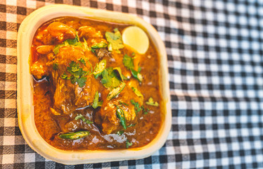 Close up of Indian Mutton curry dish in a small tray, decorated with coriander garnish.