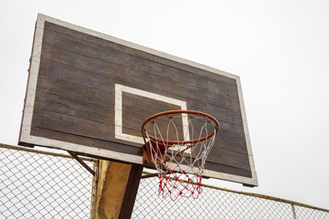 Naklejka premium Old wooden basketball hoop near iron fence.