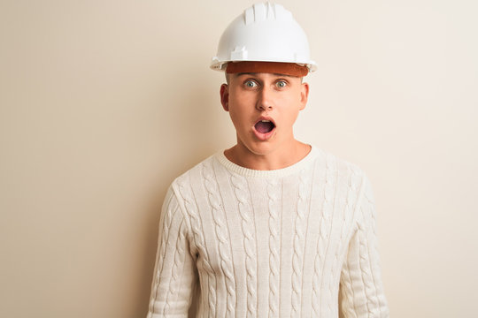 Handsome architect man wearing security helmet standing over isolated white background afraid and shocked with surprise expression, fear and excited face.