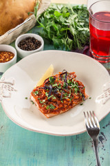 Appetizing roasted salmon steak with carrot tomato garnish on blue wooden table