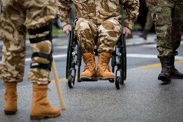 Details with a Romanian army veteran soldier, injured and disabled, sitting in a wheelchair dressed in his military desert camouflage uniform. - obrazy, fototapety, plakaty