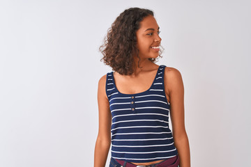 Young brazilian woman wearing striped t-shirt standing over isolated white background looking away to side with smile on face, natural expression. Laughing confident.