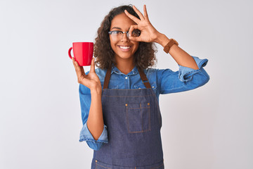 Brazilian barista woman wearing apron drinking cup of coffee over isolated white background with happy face smiling doing ok sign with hand on eye looking through fingers