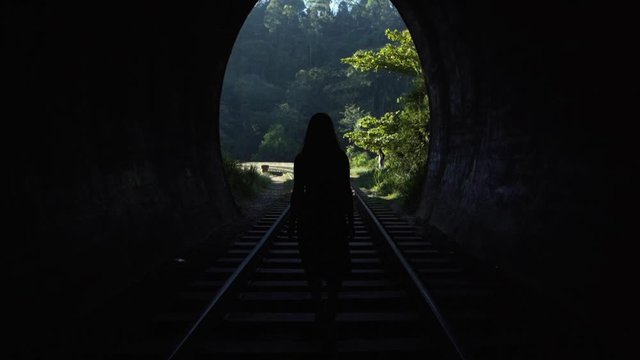 A young woman walks through a tunnel towards daylight on the railway tracks. Sri Laka.