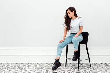 Pretty girl sitting on a chair in studio on white wall background