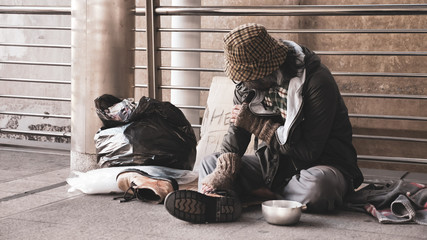 Homeless man sitting on outdoor floor.