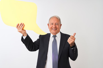 Senior grey-haired businessman holding speech bubble over isolated white background pointing and showing with thumb up to the side with happy face smiling