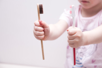 girl holding plastic and bamboo brushes in her hands, zero waste concept, environmental pollution problem