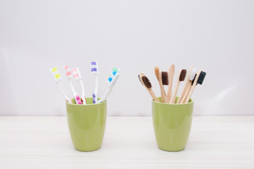 plastic and bamboo toothbrushes in green cups, light background, copy space, eco friendly material concept