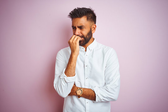 Young indian businessman wearing elegant shirt standing over isolated pink background looking stressed and nervous with hands on mouth biting nails. Anxiety problem.