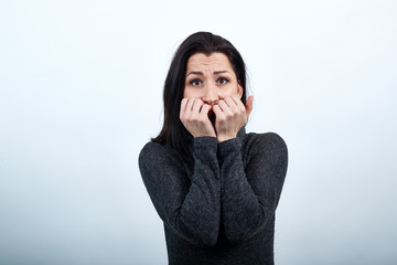 Scared young woman in fashion black sweater over isolated white background, biting nails, looking frightened. Lifestyle concept