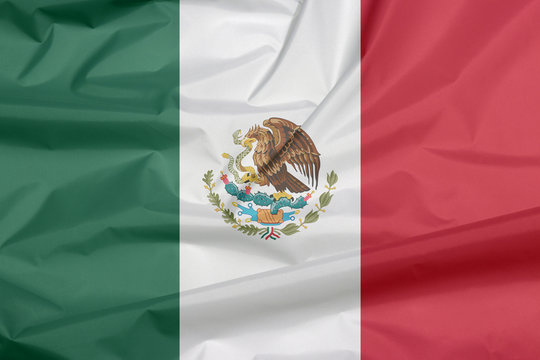 Crease of Mexican flag background, a vertical tricolor of green white and red with the nation Coat of Arms centered on white.