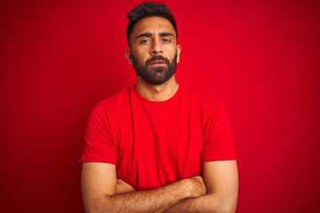Young handsome indian man wearing t-shirt over isolated red background skeptic and nervous, disapproving expression on face with crossed arms. Negative person.