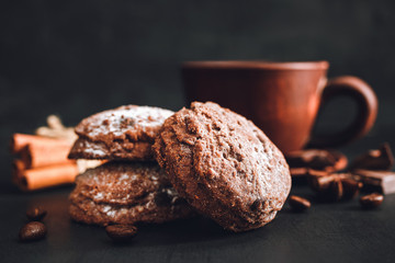Chocolate cookies with powdered sugar and brown cup with hot coffee on dark background